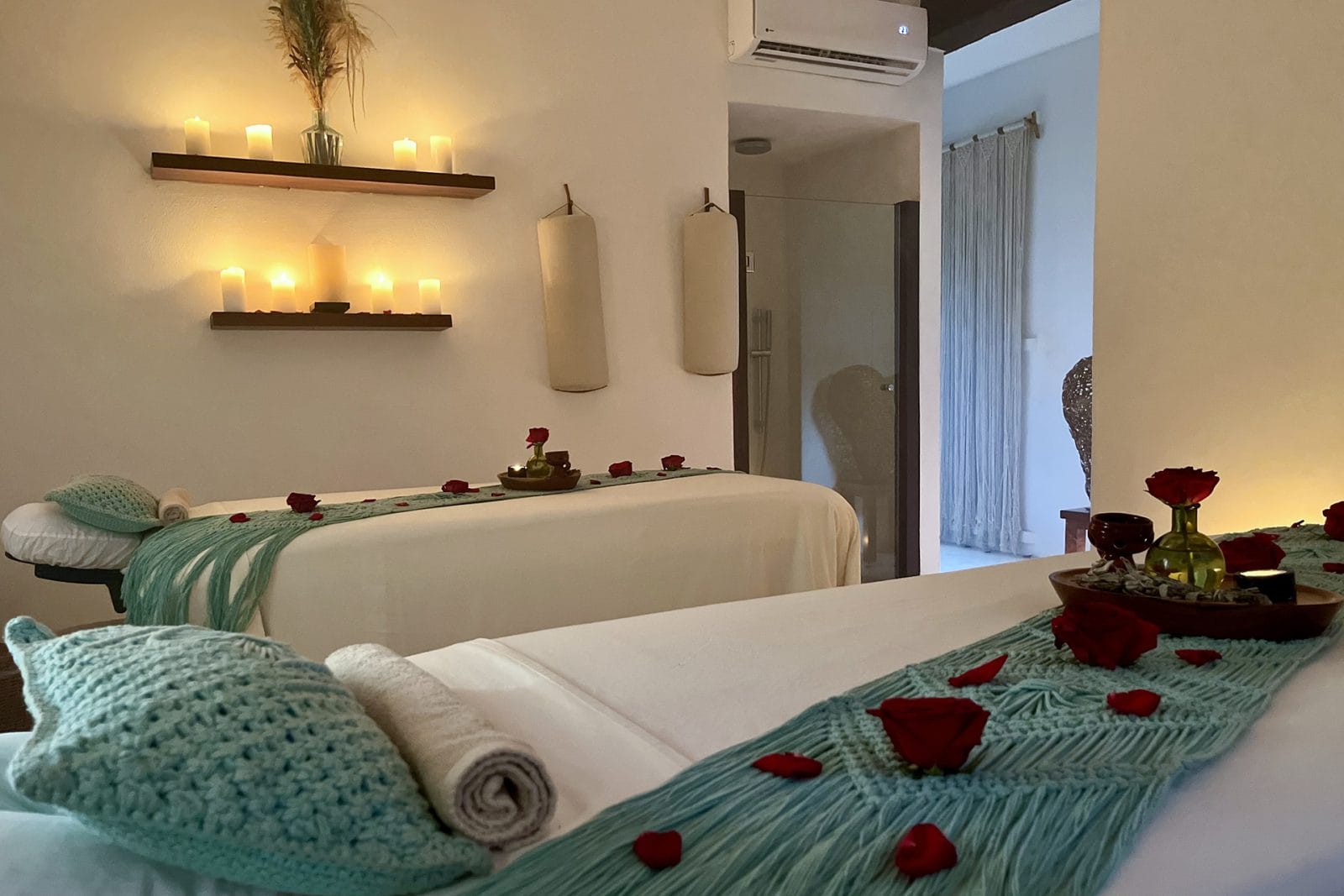 Two massage beds decorated with rose petals and surrounded by candlelight in a couple's treatment room at Naj Naay Spa, Tulum, with organic oils ready for use.