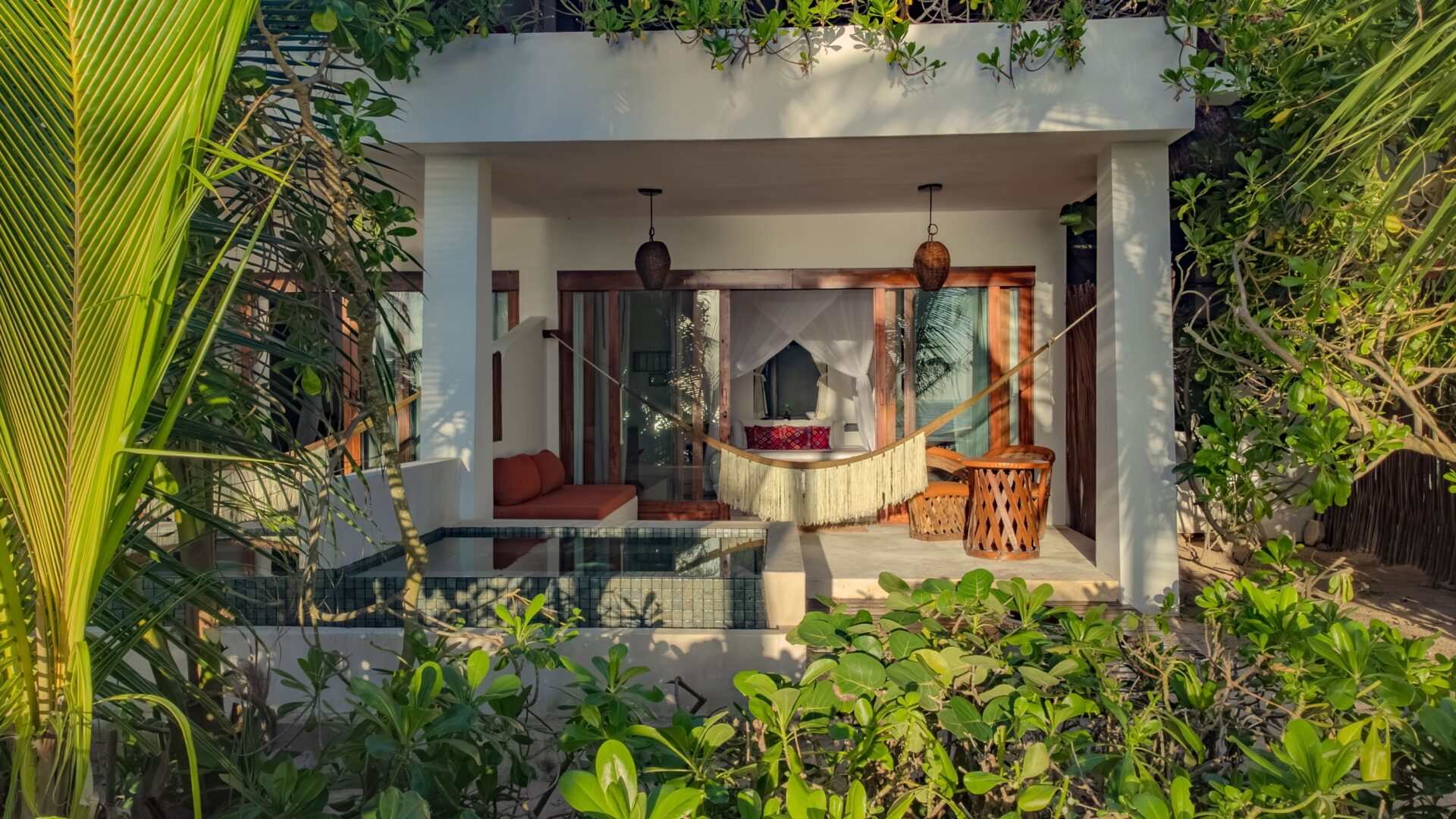 A Deluxe room patio with private plunge pool, hammock, sofa and table and chairs. The canopied kink size beds opens on the patio.