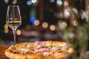 A mortadella pizza with a glass of white wine