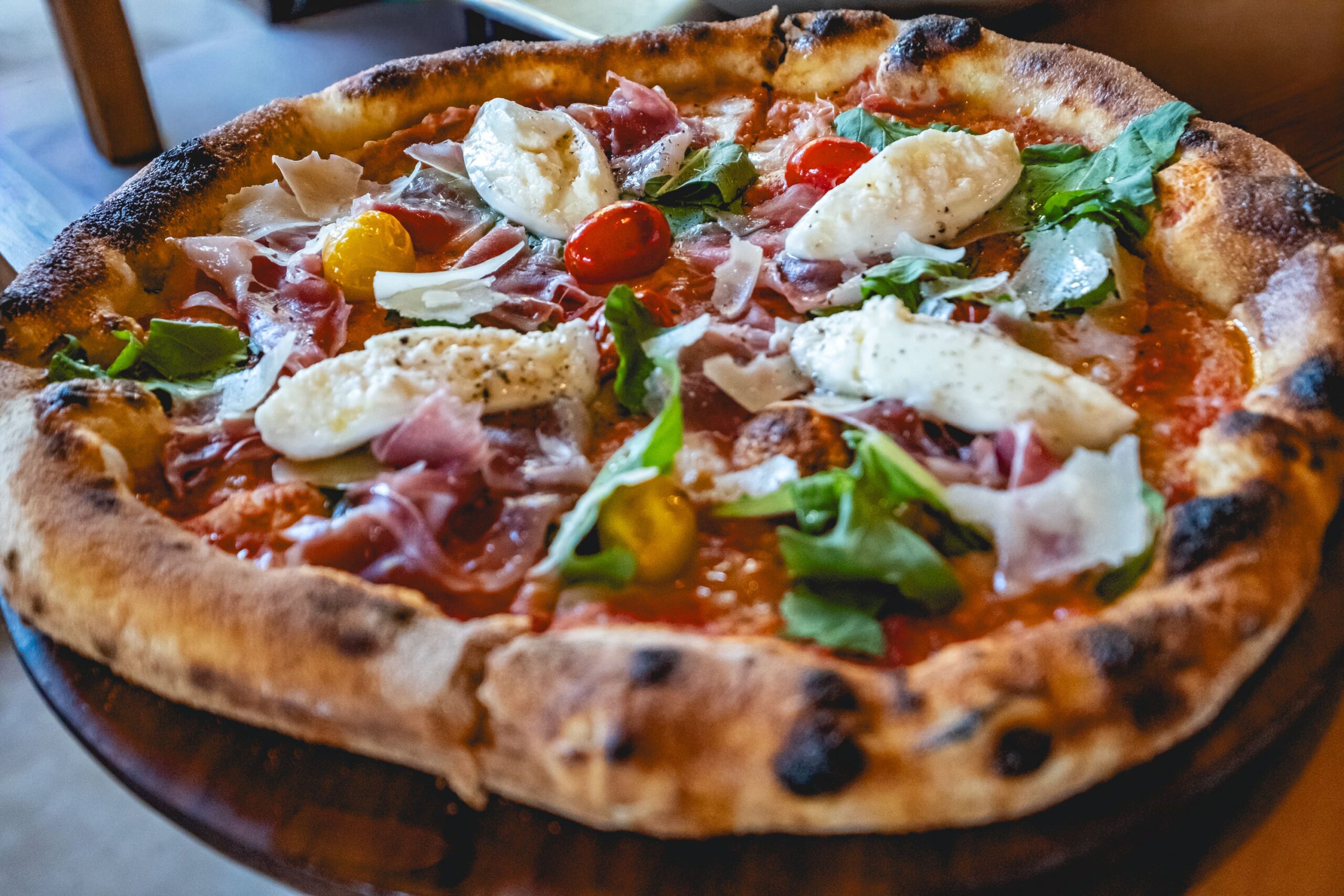 Pizza with San Marzano tomato DOP, fior di latte mozzarella, arugula, confit tomatoes, Parma ham, Parmigiano reggiano.
