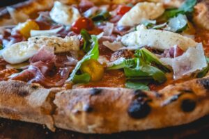 A close up of a prosciutto di parma pizza with San Marzano tomato DOP, fior di latte mozzarella, arugula, confit tomatoes, Parma ham, Parmigiano reggiano.