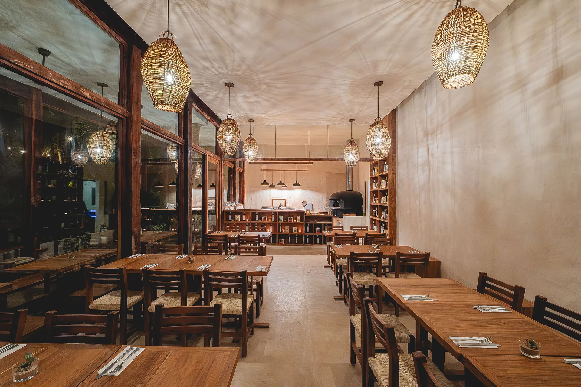 Inside of Autentico restaurant with wooden tables and soft lighting. Pizza oven on the far end