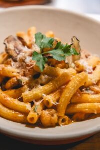 A plate of sedanini alla norma withCherry tomatoe, golden fried eggplants, pecorino romano, basil, garlic and onion
